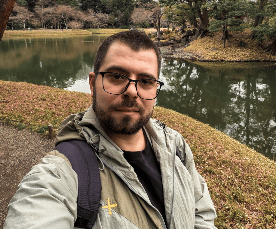 Goksel by a pond in a Japanese garden, autumn trees behind.