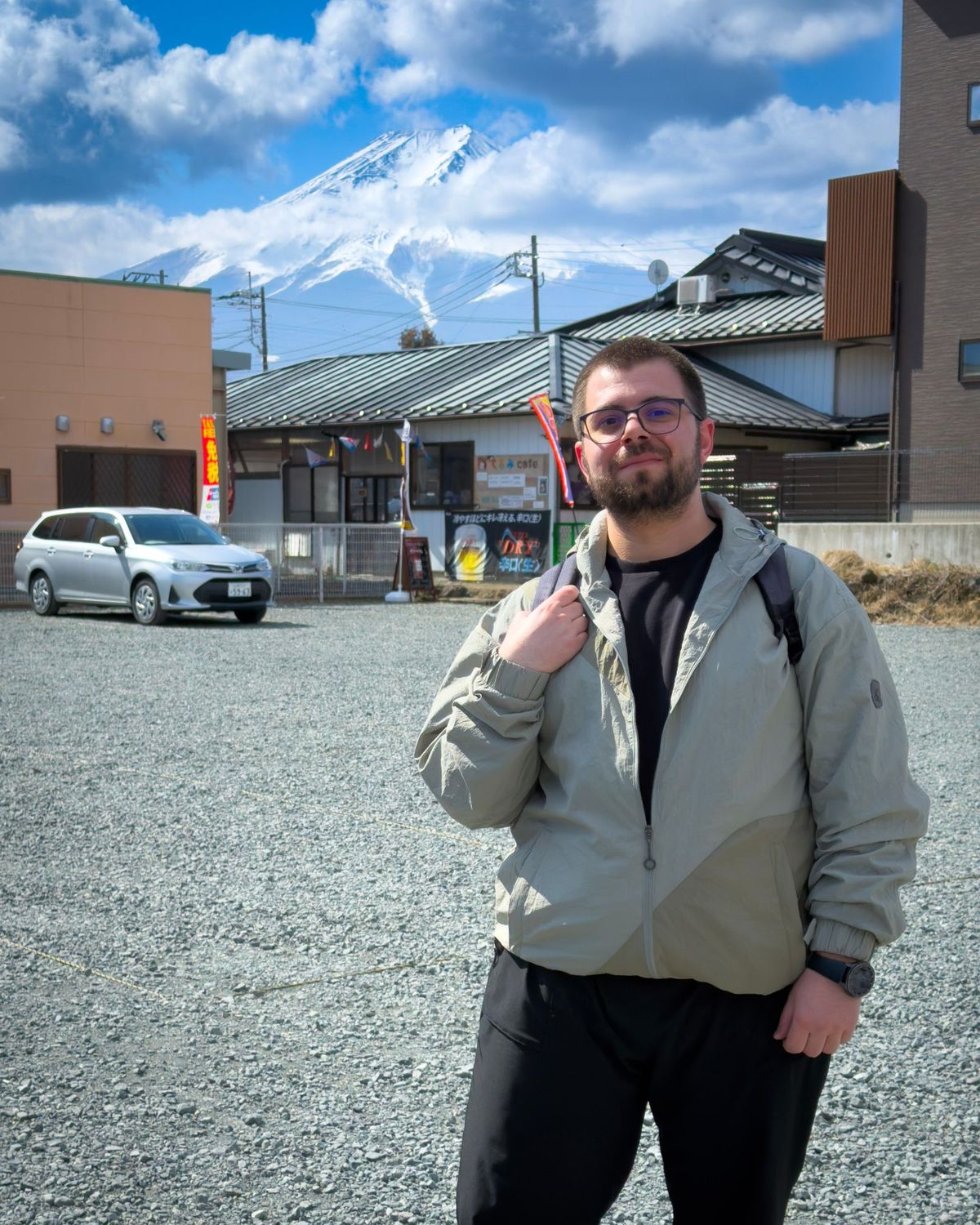 Goksel smiling in front of a snow-capped Mount Fuji rising behind small houses in Yamanashi.