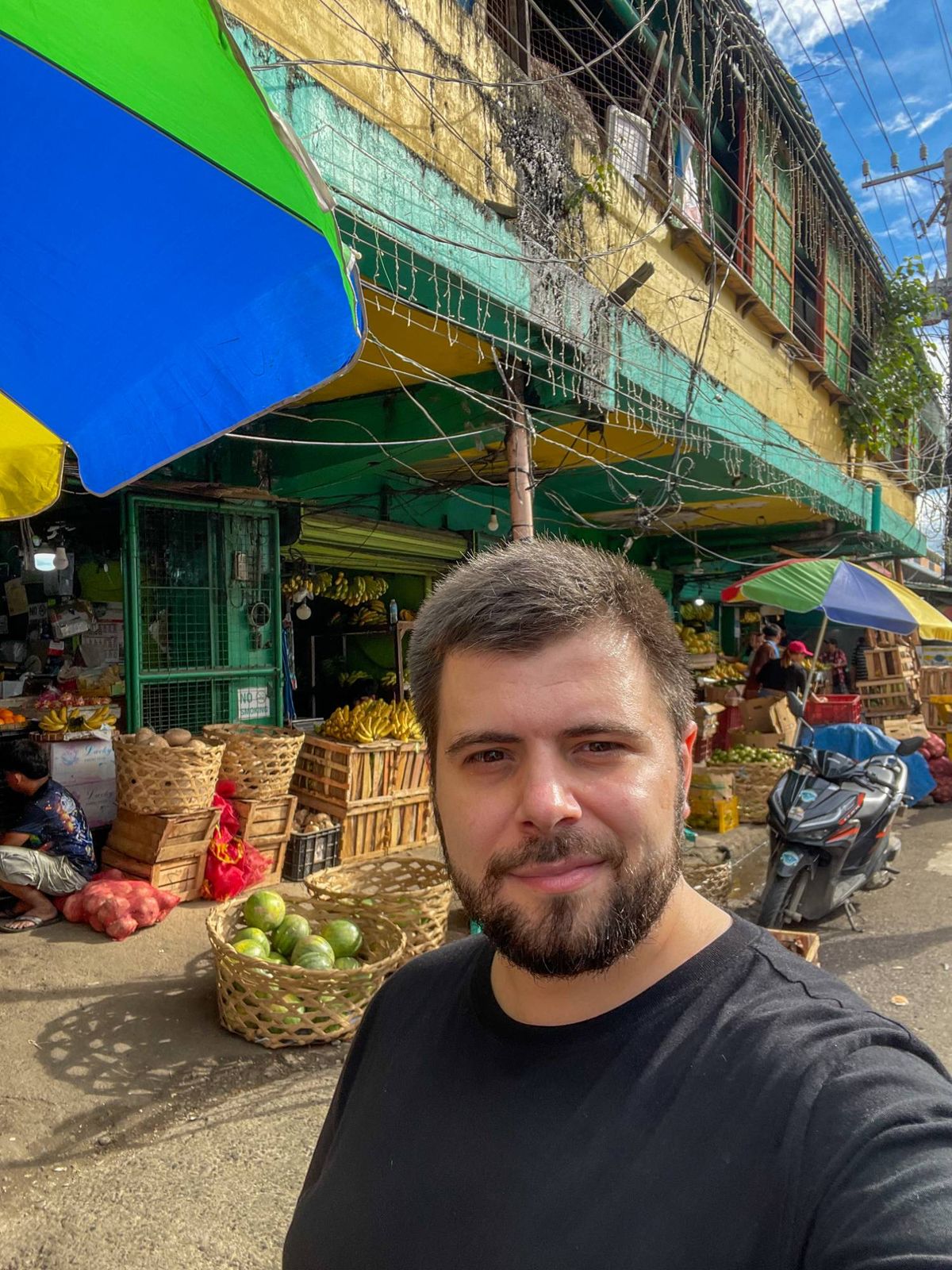 Goksel taking a selfie in front of fruit stalls and a green and yellow building at Colon Market in Cebu.