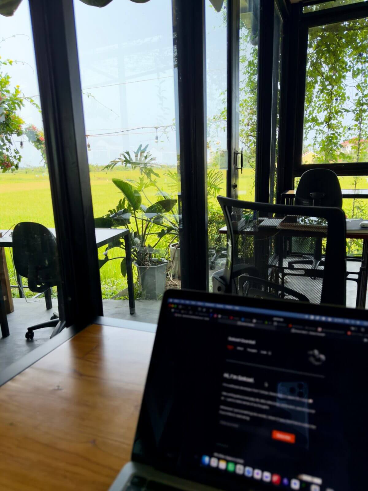 Laptop on a wooden desk by the windows with rice fields outside at Hub Hoi An