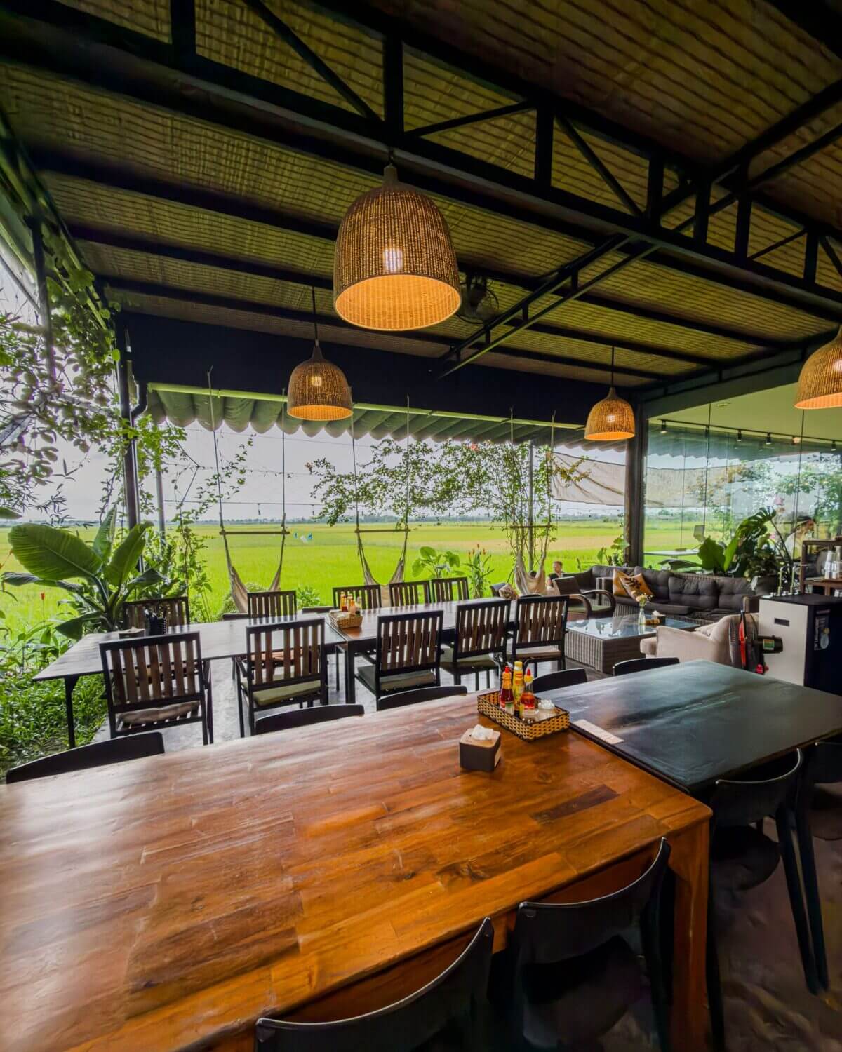 Wooden dining tables under woven pendant lamps with a view of the rice fields at Hub Hoi An