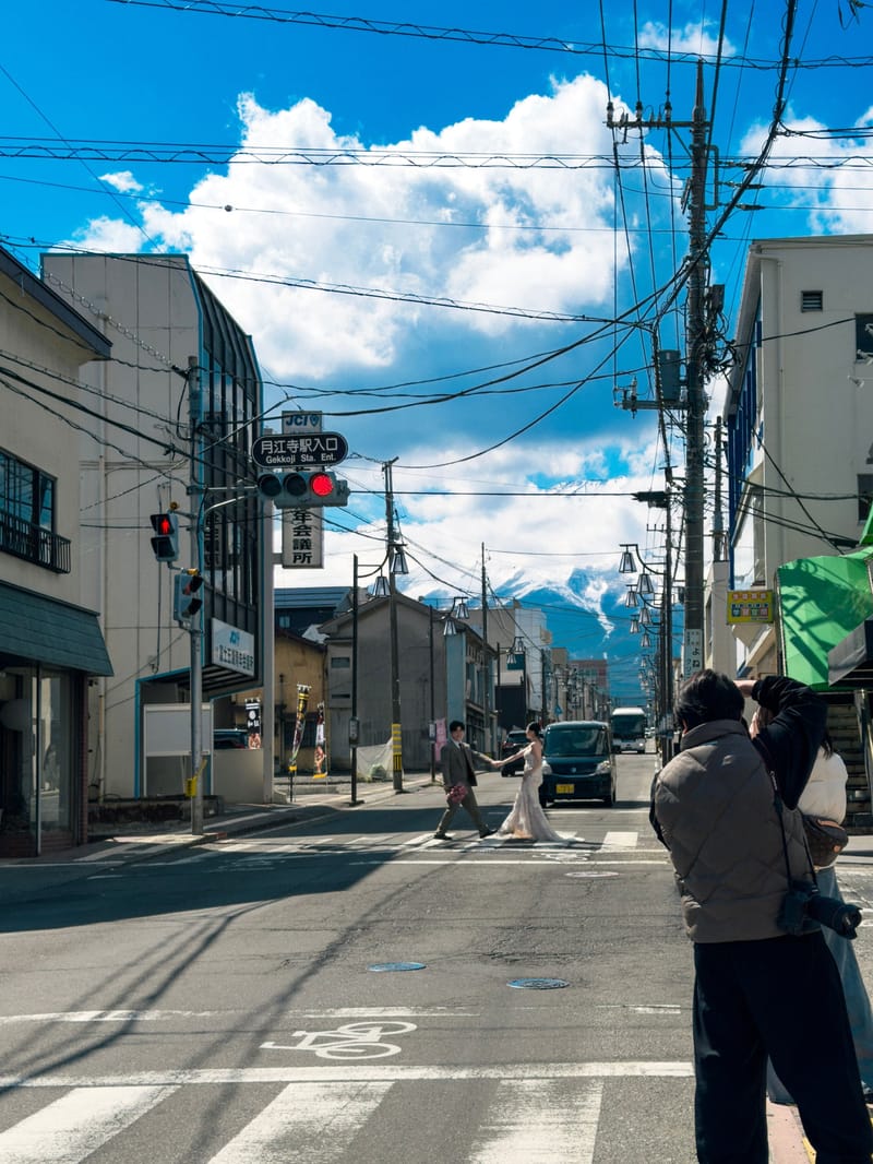 People cross a quiet street; a snow-capped mountain rises at the end of the road.
