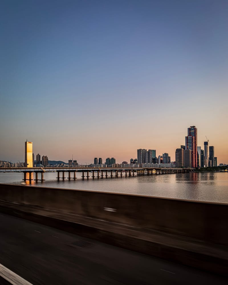 The Seoul skyline and a long bridge over the Han River at sunset.