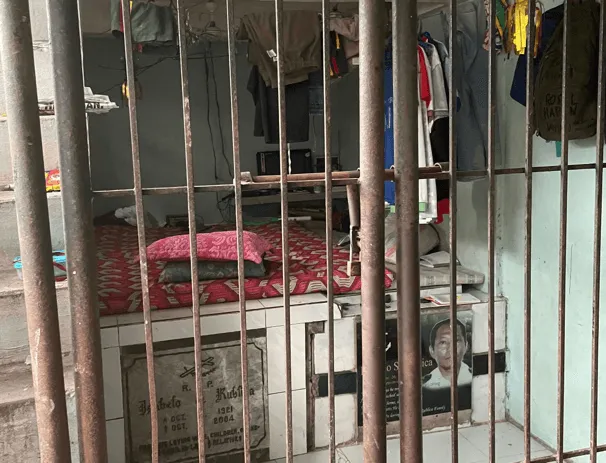 A small room built against a grave at Carreta Cemetery, seen through rusted bars.