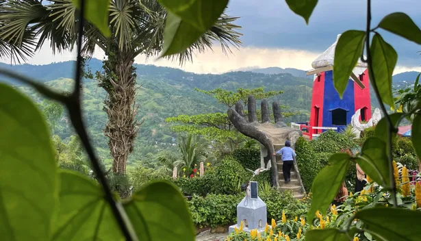Sirao Garden in Cebu, with a stone hand sculpture, a red and blue tower, and green hills.