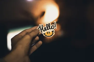 A hand holding a small sticker that says Hello, against a warm blurred light.